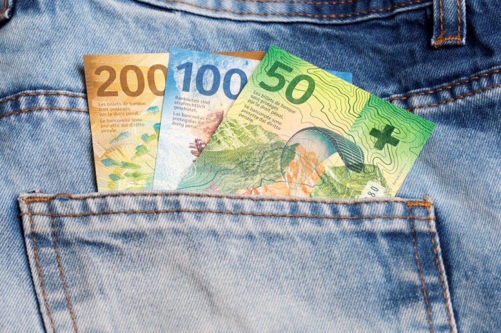 Swiss franc banknotes tucked in the pocket of blue jeans, symbolizing Swiss banking costs and financial security.