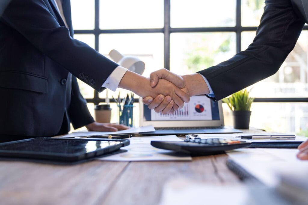 Business professionals shaking hands after an M&A deal to move exit proceeds into offshore banking structures.