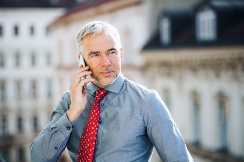 An experienced wealth management professional talking on a smartphone, representing the private strategy call used to assess client profiles and shortlist Swiss banks.