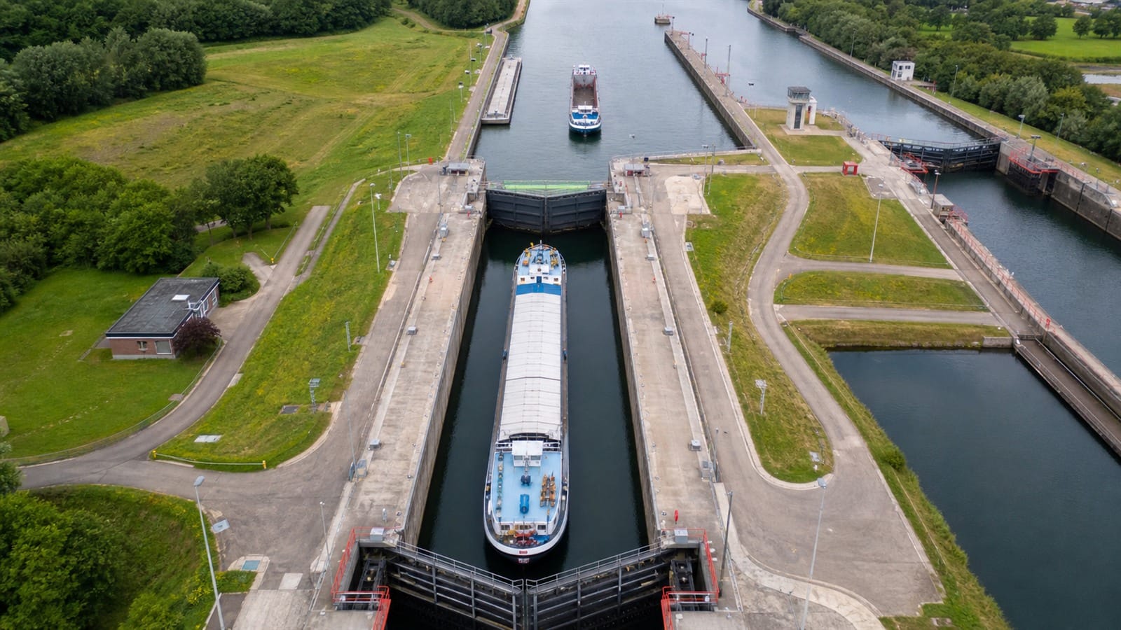 Commercial vessels passing through a controlled canal lock with another vessel waiting